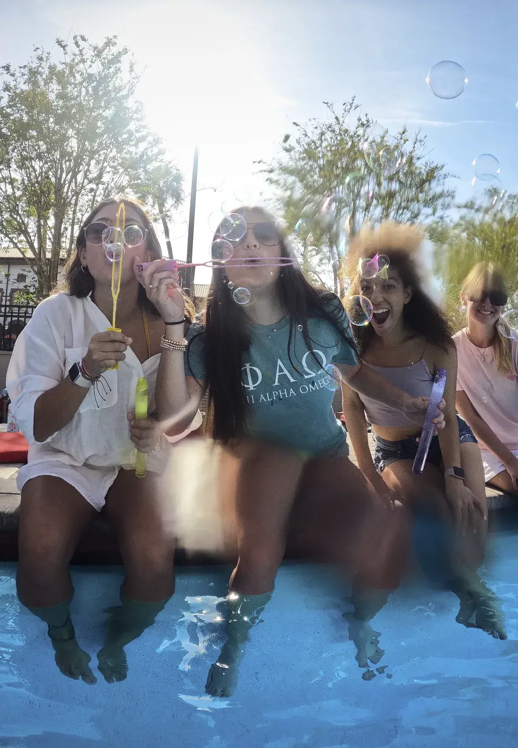 Students sitting pool-side, blowing soap bubbles over the water