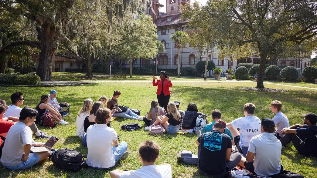 A professor teaching to their class of students who are sitting on the grass of the West Lawn