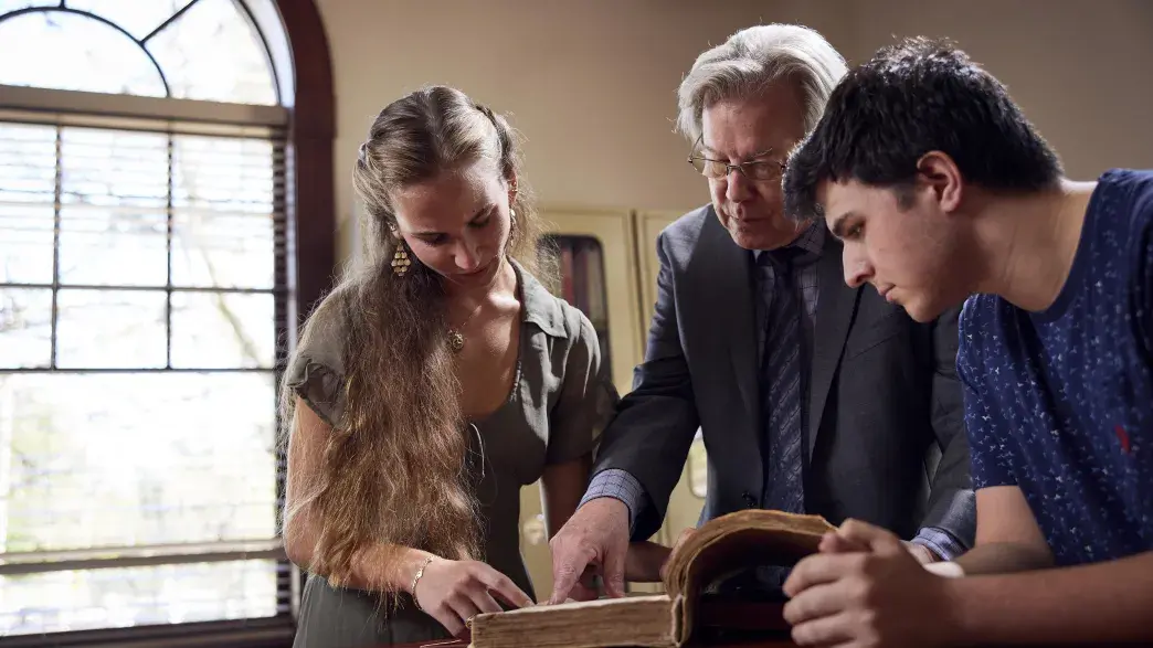 Two students and a professor examine a thick book.