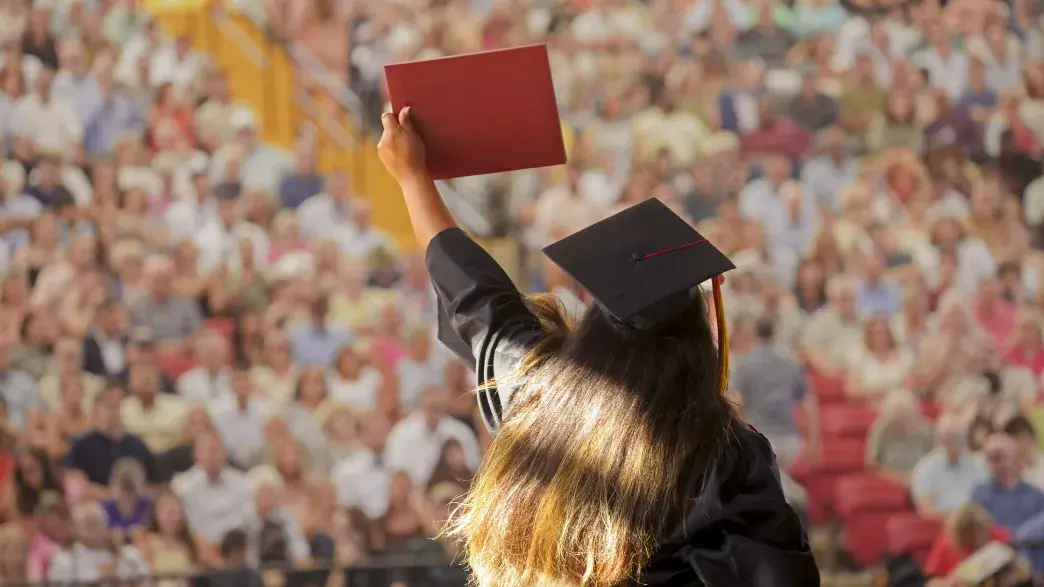 Student crossing stage at graduation, holding up diploma