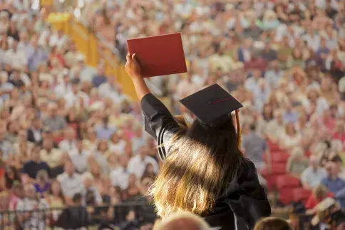 Student crossing stage at graduation, holding up diploma