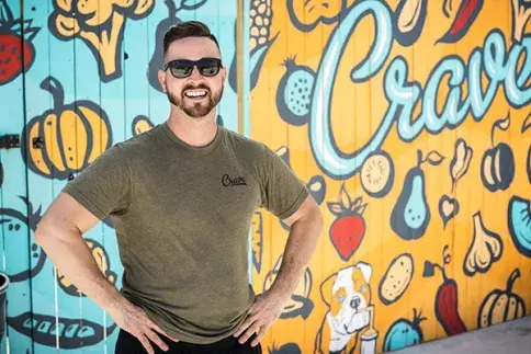 Flagler alum and business owner stands in front of sign for Crave food truck. 