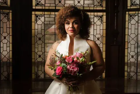 A bride is holding flowers and standing in front of a stained glass window.