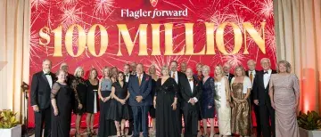 A group shot of Flagler College President Delaney and friends in front of a large banner that reads 'Flagler Forward $100 Million' at the celebration gala.