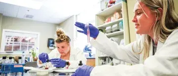 Students wearing lab coats and gloves working in the science lab