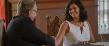 President Delaney and Christina Valdés shake hands seated at a table