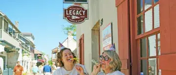 Nikki L. and Sam P. posing in front of the Legacy with 25th anniversary t-shirts and birthday hats