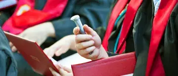 Spike and diploma in the hand of sitting graduate at a recent Commencement