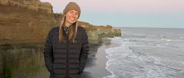 Student Katie Kress poses for a photo on the New Zealand cliffside with the ocean behind her