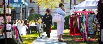 A shot down a sidewalk with Mini Mane Market booths on each side of the sidewalk. Two students stand browsing the market.