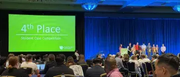 Ballroom full of people at table and students on stage accepting an award