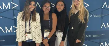 Four students pose for a photo in front of a AMA branded backdrop