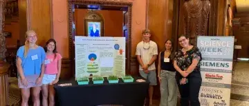 Students standing by their public research showcase table in the Ponce rotunda