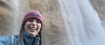 Amelie Thompson smiles for a selfie with a waterfall behind her