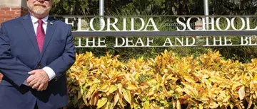 Flagler College Alum, Owen McCaul, stands next to the sign for the Florida School for the Deaf and the Blind