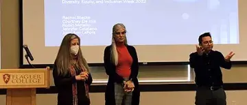 Flagler Professors June Ann LeFors and Jennifer Catalano stand in front of a project screen for a presentation.