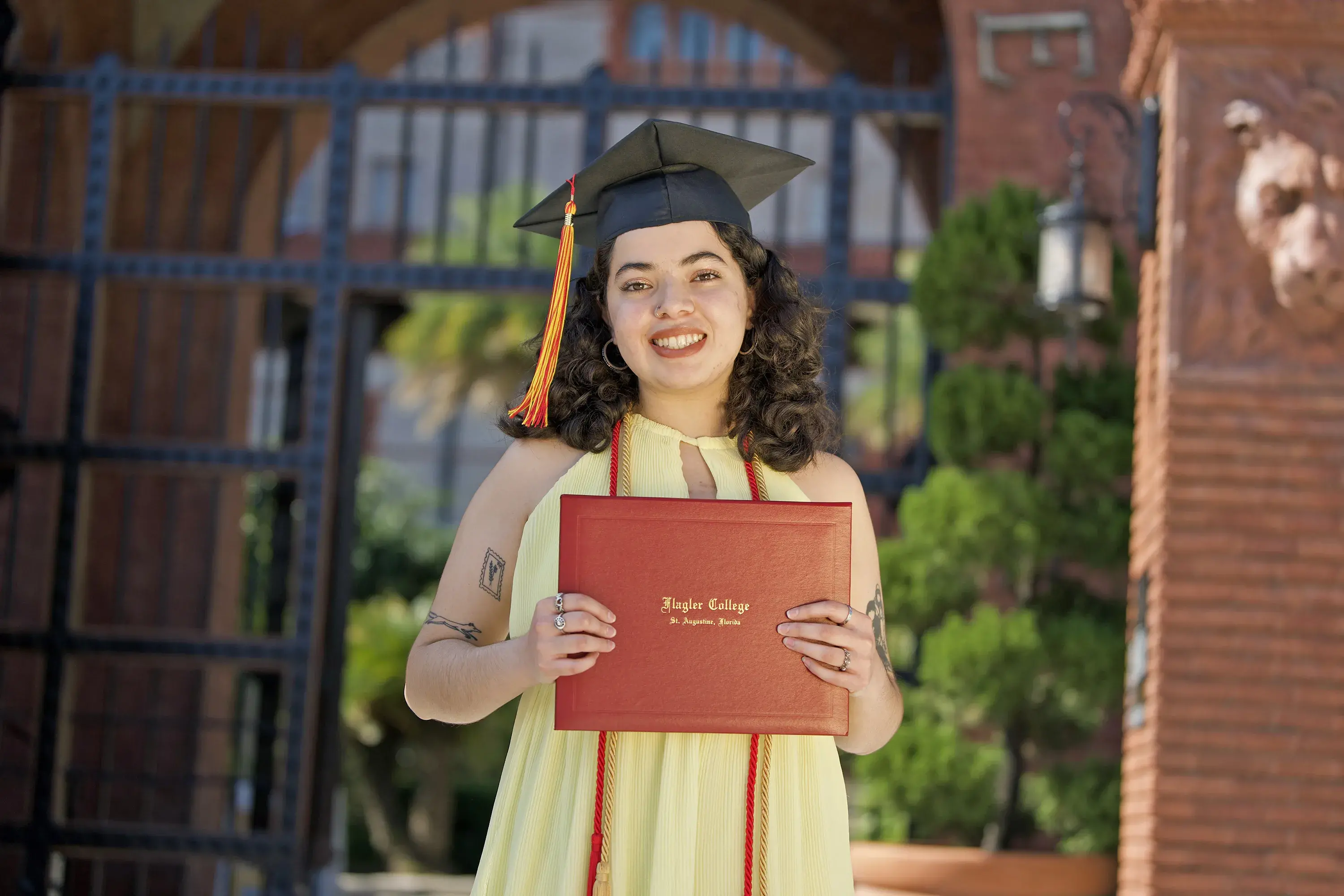 Alana holding diploma in front of courtyard gates