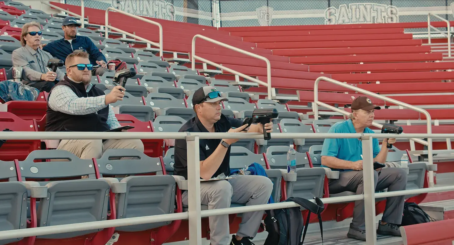 Baseball scouts pointing radars at the field from the Drysdale Stadium bleachers