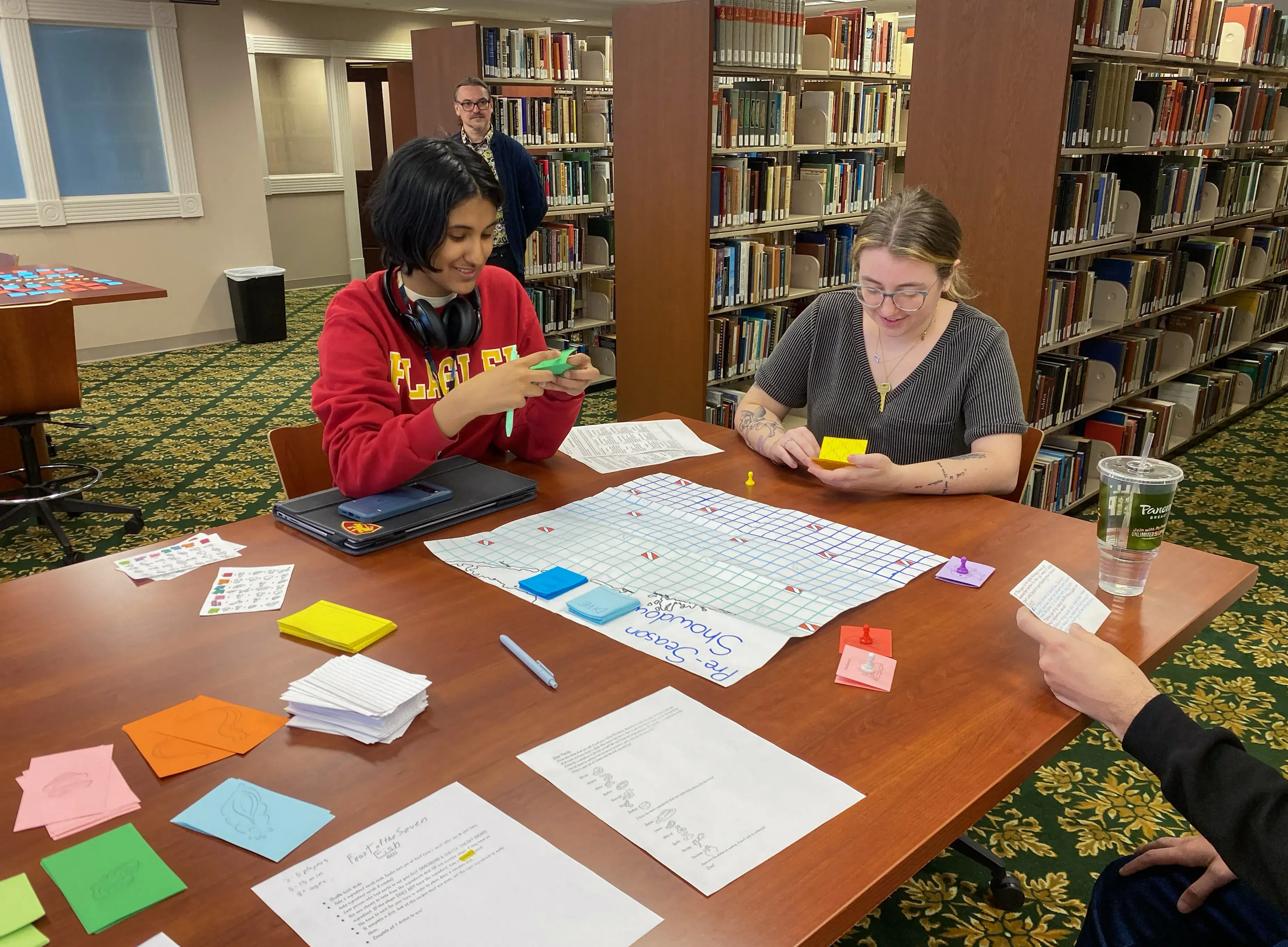 Peer group playing student-made game while Moody stands behind to observe