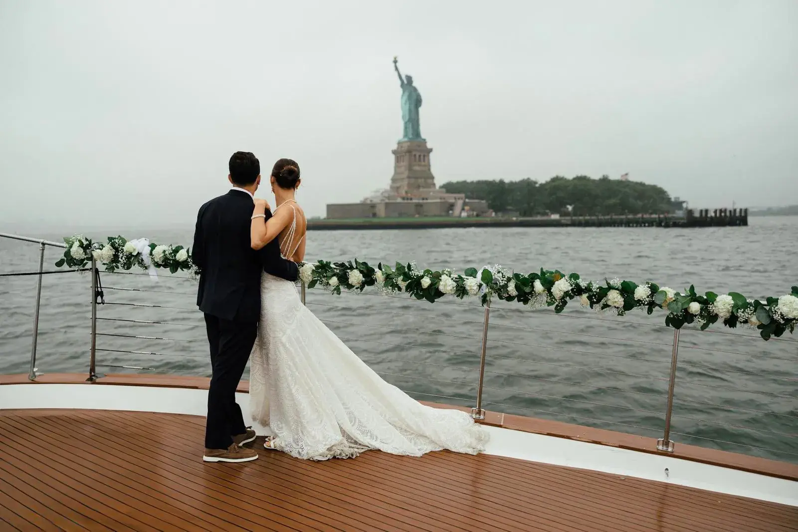 Marietta and husband pose on boat in front of statue of liberty on wedding day