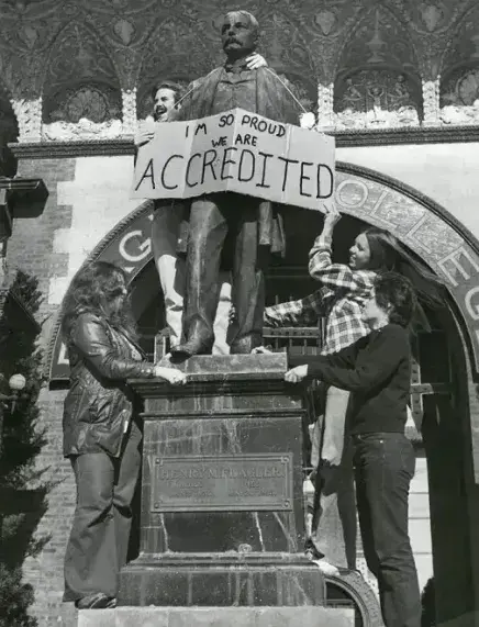 Students celebrating accredidation with sign on the Henry Flagler that reads "I'm so proud we are accredited" statue