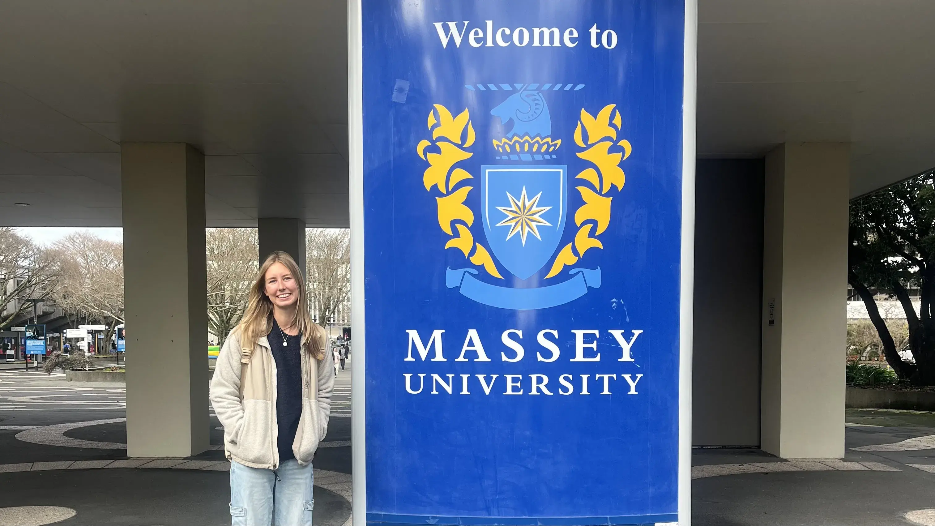 Katie Kress stands in front of a sign for Massey University in New Zealand