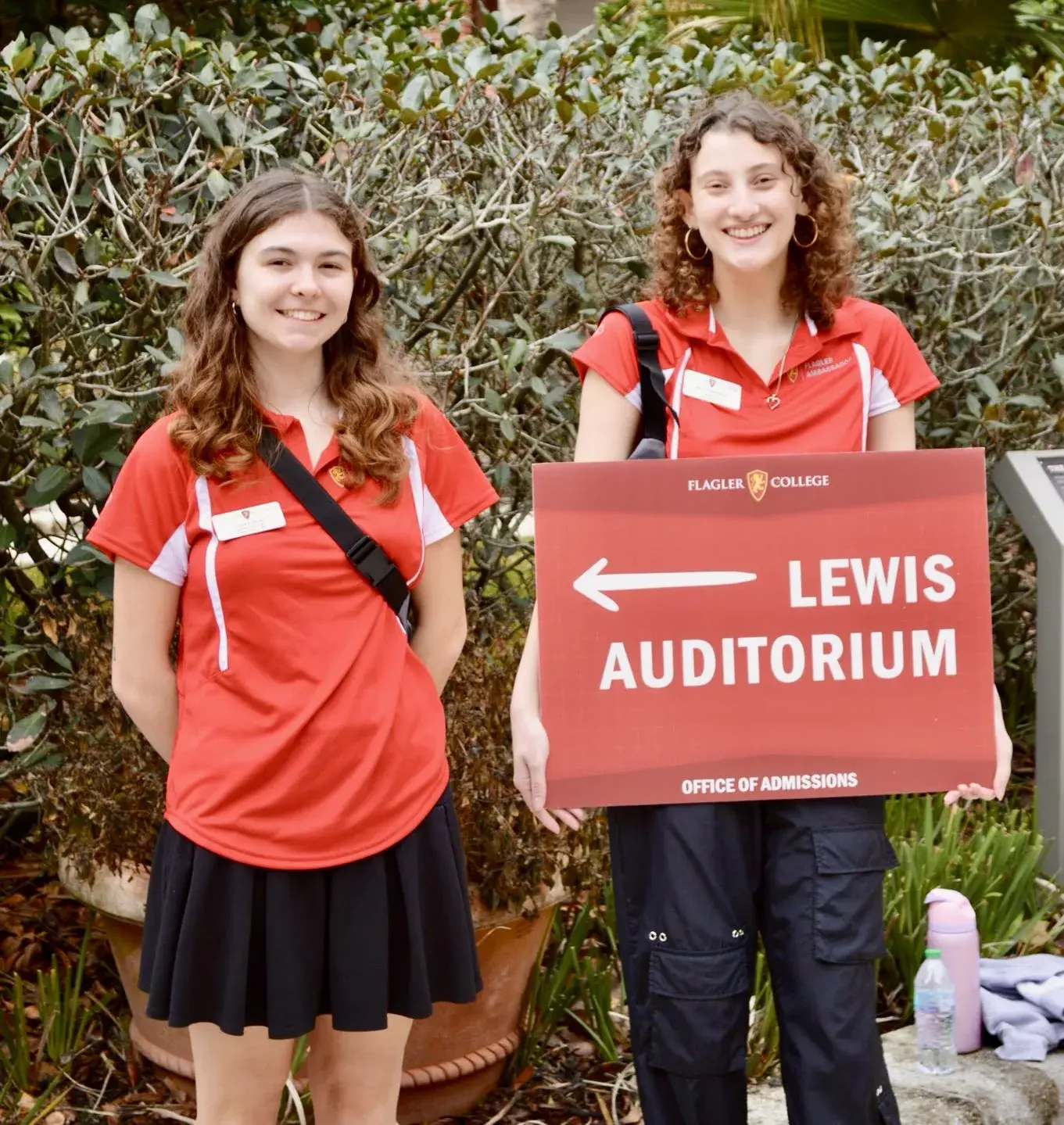 Two student ambassadors pose for a photo with one of them holding a sign directing families to Lewis Auditorium