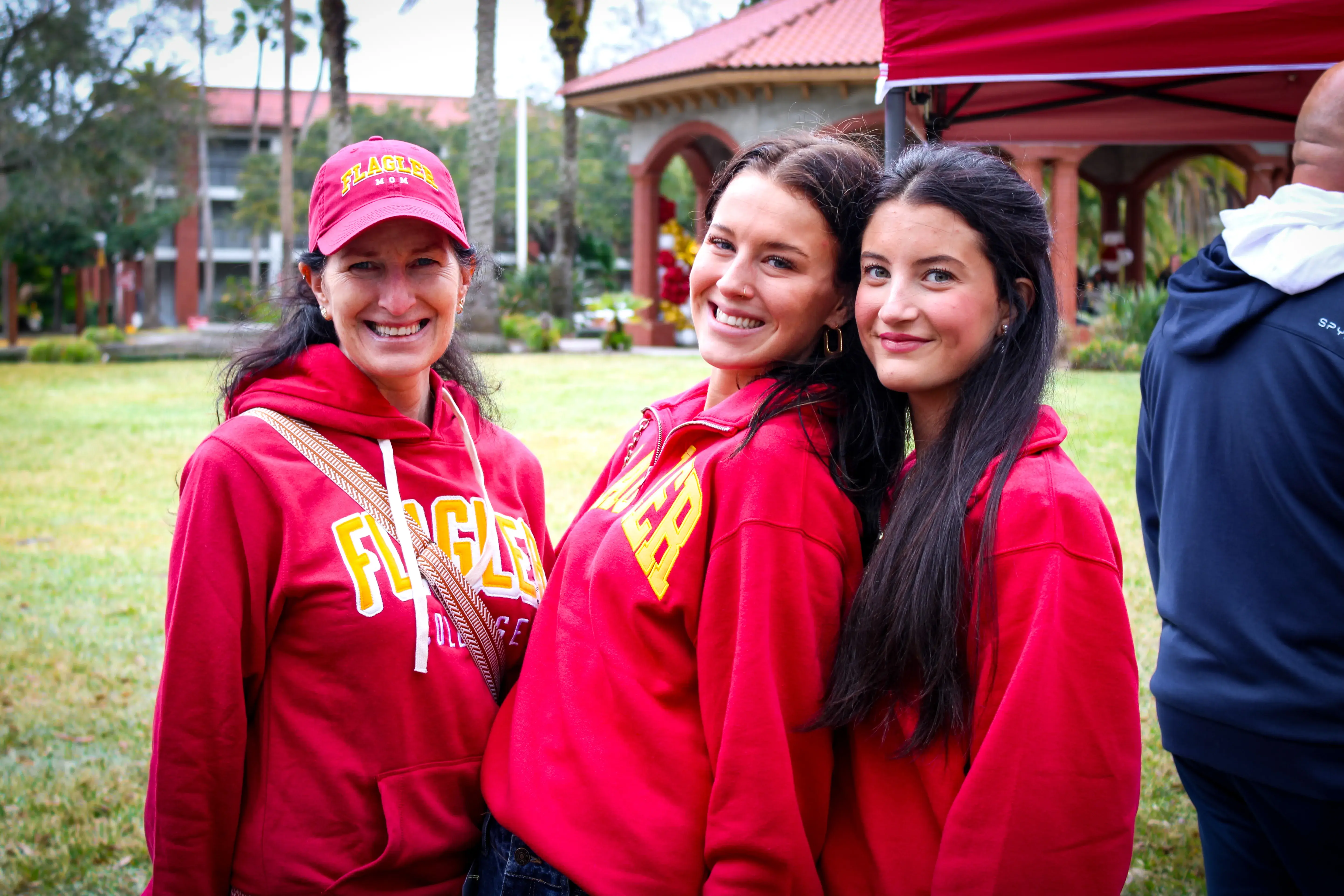Two newly accepted students and one of their moms pose for a picture wearing matching red Flagler sweaters