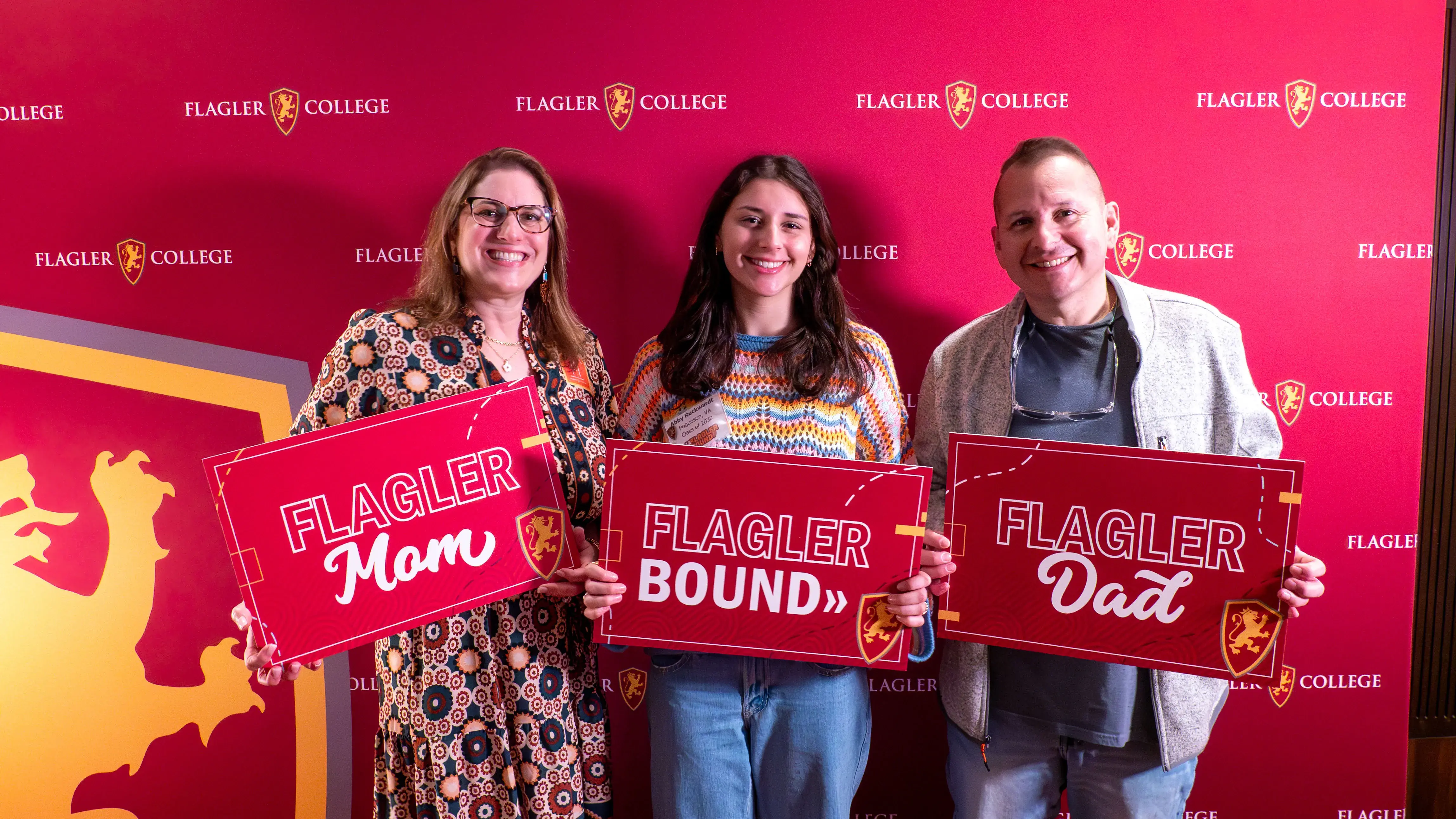An incoming student and her family pose for a picture in front of a Flagler themed backdrop
