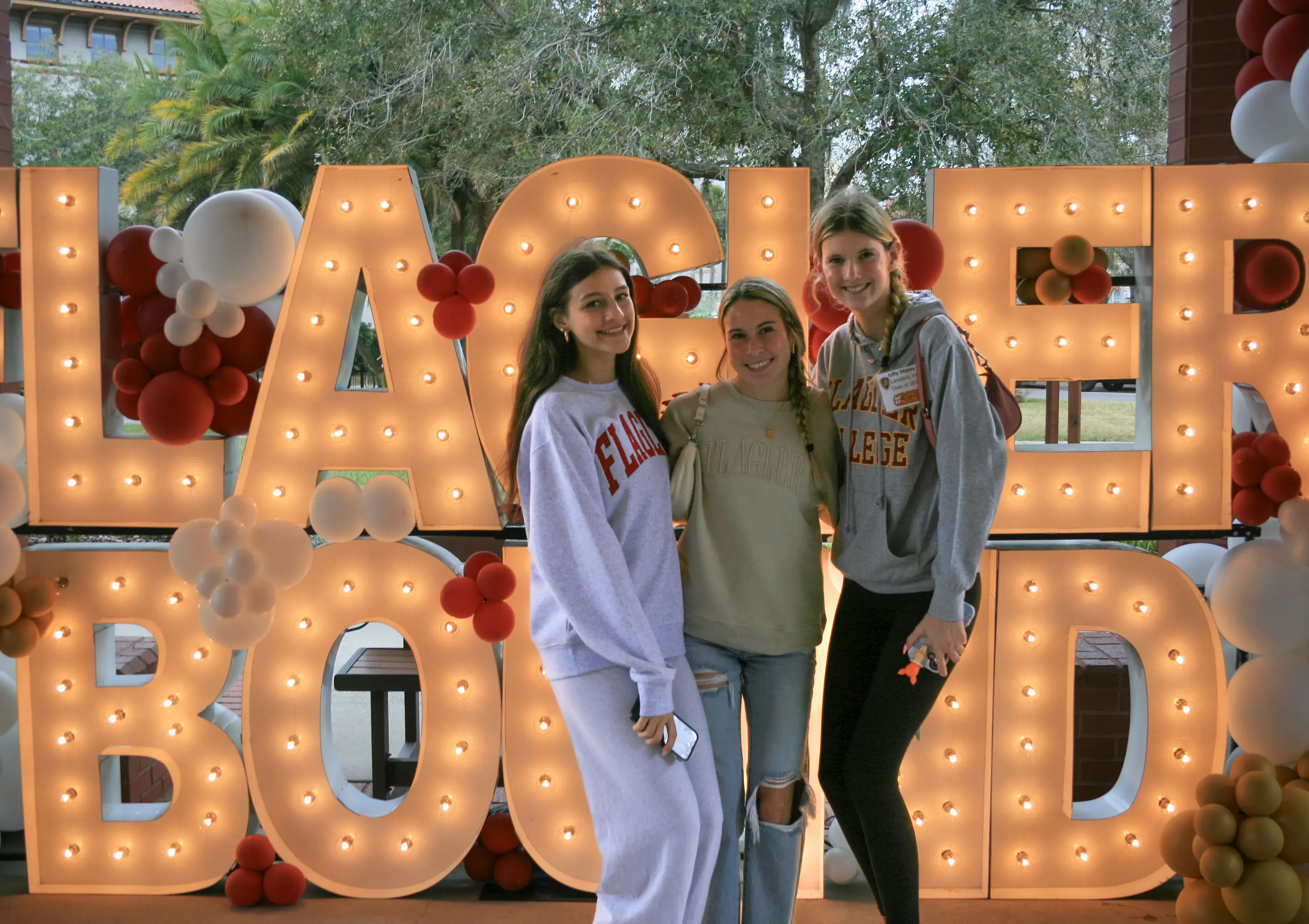 Prospective students stand in front of a Flagler Bound light up sign