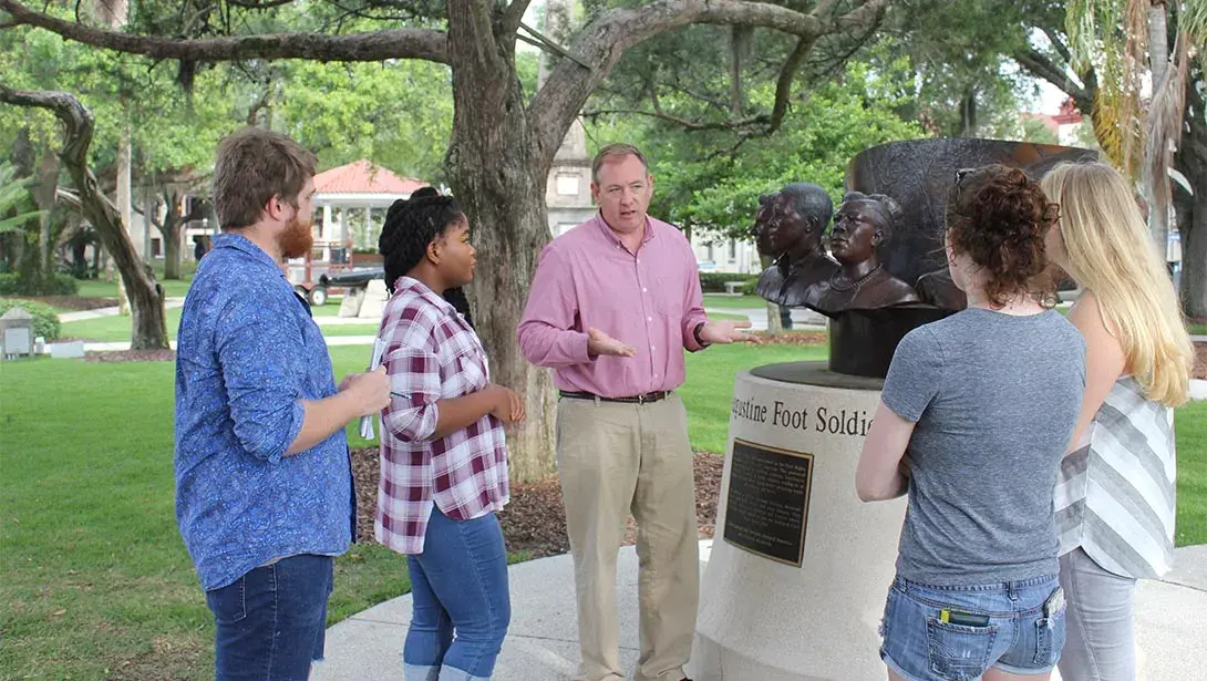 Student and professor gather around St. Augustine Foot Soldiers monument. 