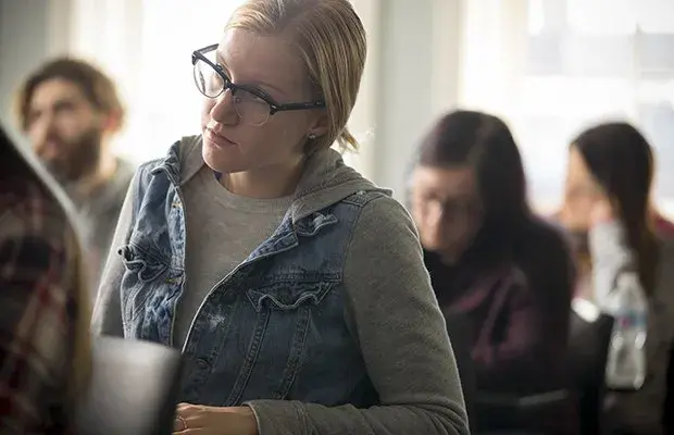 Seated student in glasses looks towards professor. 